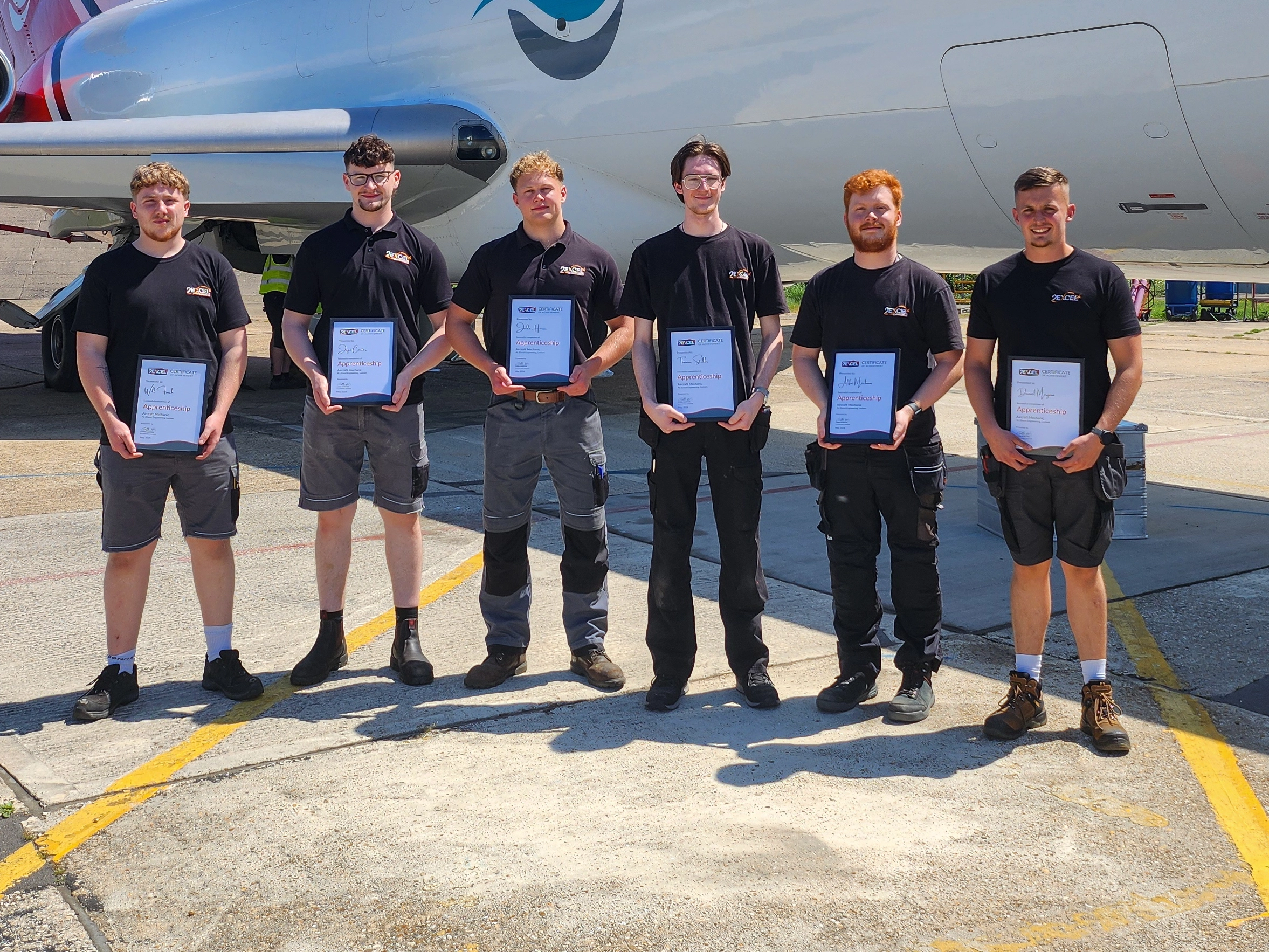 group of men dressed in black beside a red and white aircraft and they are holding framed certificates