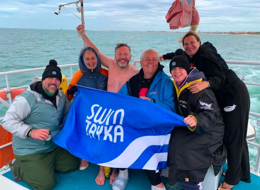 Group of people on a boat holding a blue SwimTayka flag